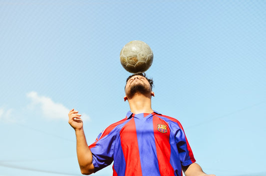 un-homme-tient-un-ballon-de-football-en-equilibre-sur-sa-tete-bNVq5OEzYgY